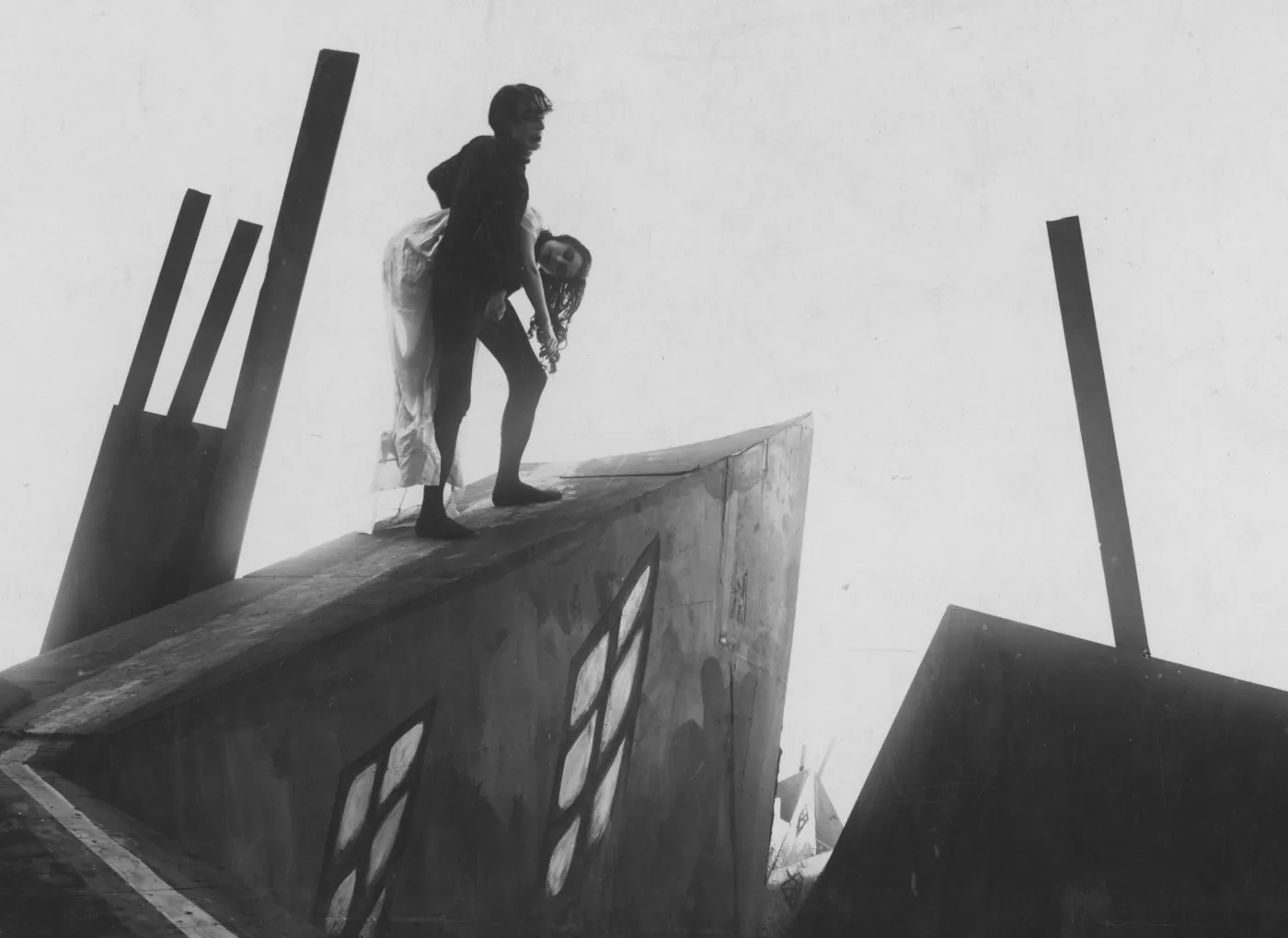 Homem uma mulher enquanto sobe uma rampa. A imagem está em preto e branco e o cenário é composto por formas extremamente agudas e abstratas.