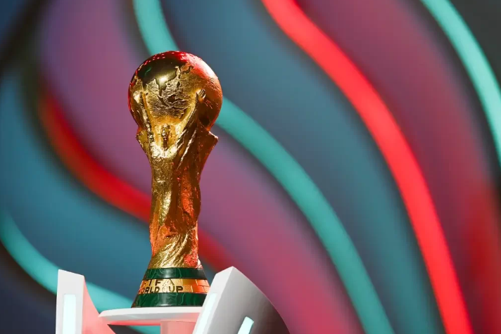 Foto registra a taça da Copa do Mundo da Fifa, em um fundo verde e vermelho.