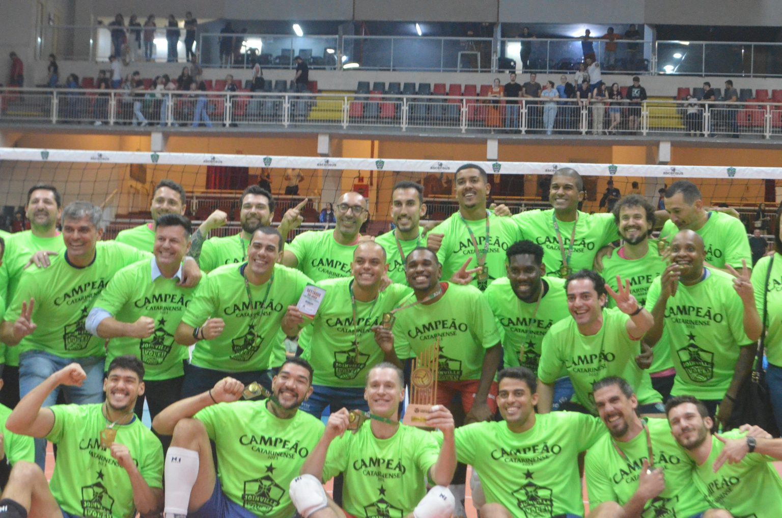 Jogadores do Joinville Vôlei comemorando título inédito, todos com camisas verdes.