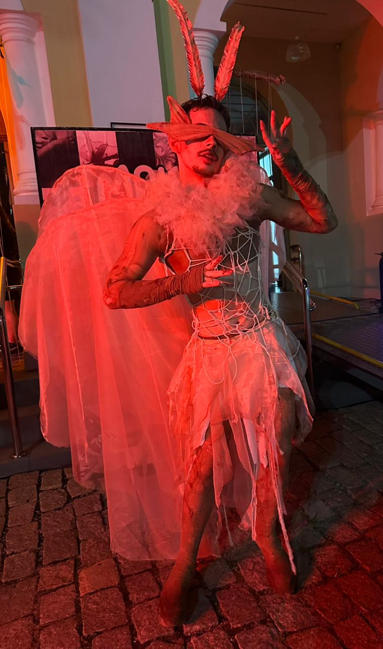Arthur está vestido com um figurino com asas esvoaçantes na cor branca, feitas de tecido, uma saia curta com cortes irregulares na cor branca. Na parte de cima, veste uma espécie de corpete com detalhes de cordas soltas. Usa uma venda em formato triangular, imitando os olhos da mariposa e duas antenas compridas na cabeça, parecendo duas penas. No pescoço um tecido volumoso contorna o busto.
