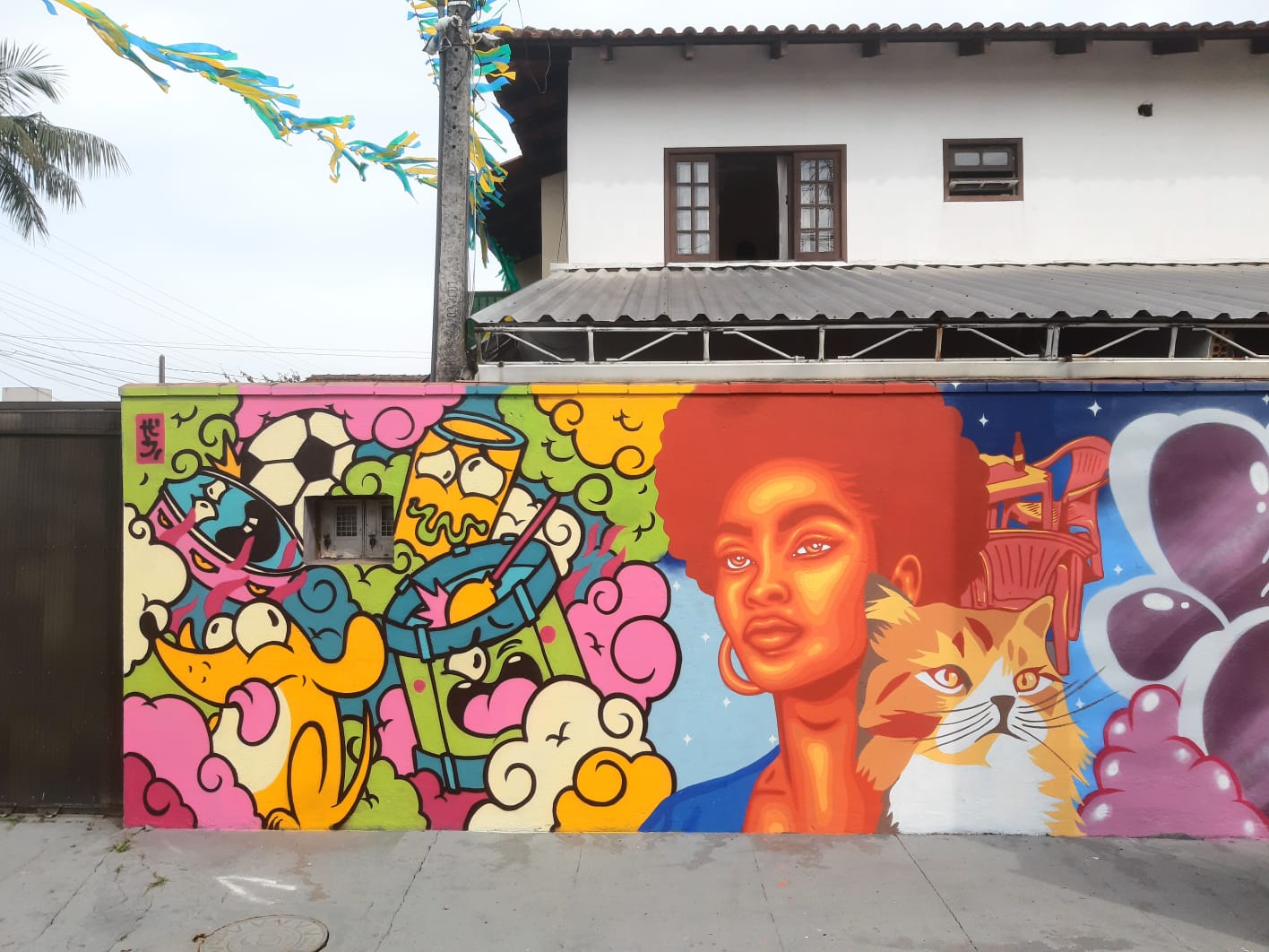 Mural artístico colorido em parede residencial com ilustrações de personagens, formas abstratas, uma figura feminina e um gato 
