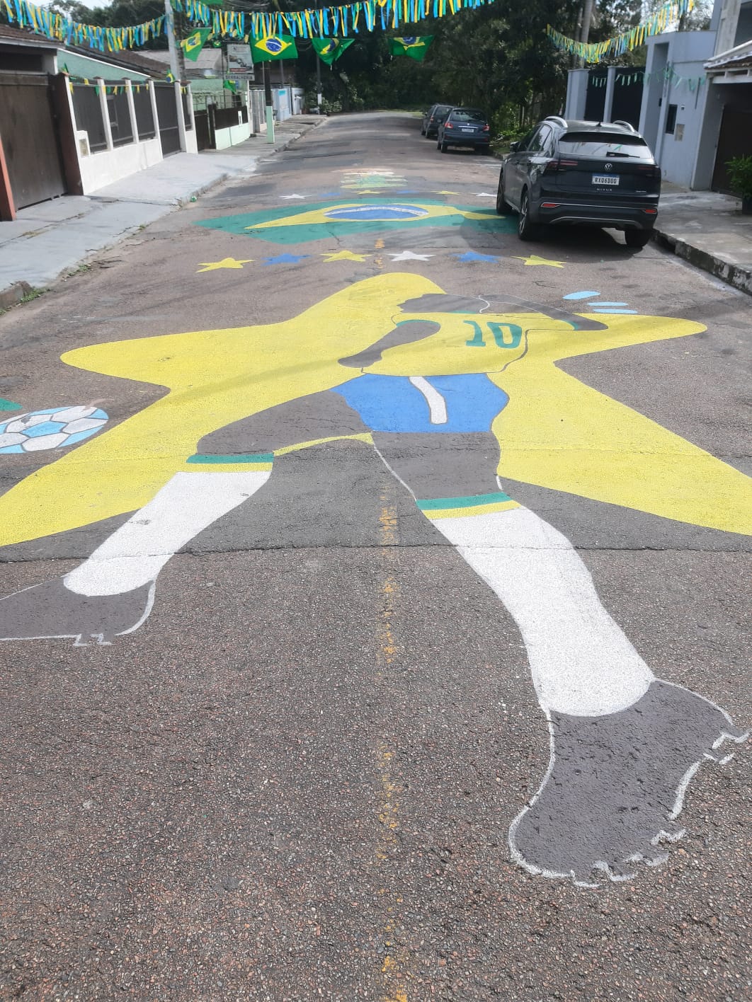Pintura de jogador de futebol com camisa da seleção brasileira representada no asfalto de uma rua decorada para a Copa do Mundo