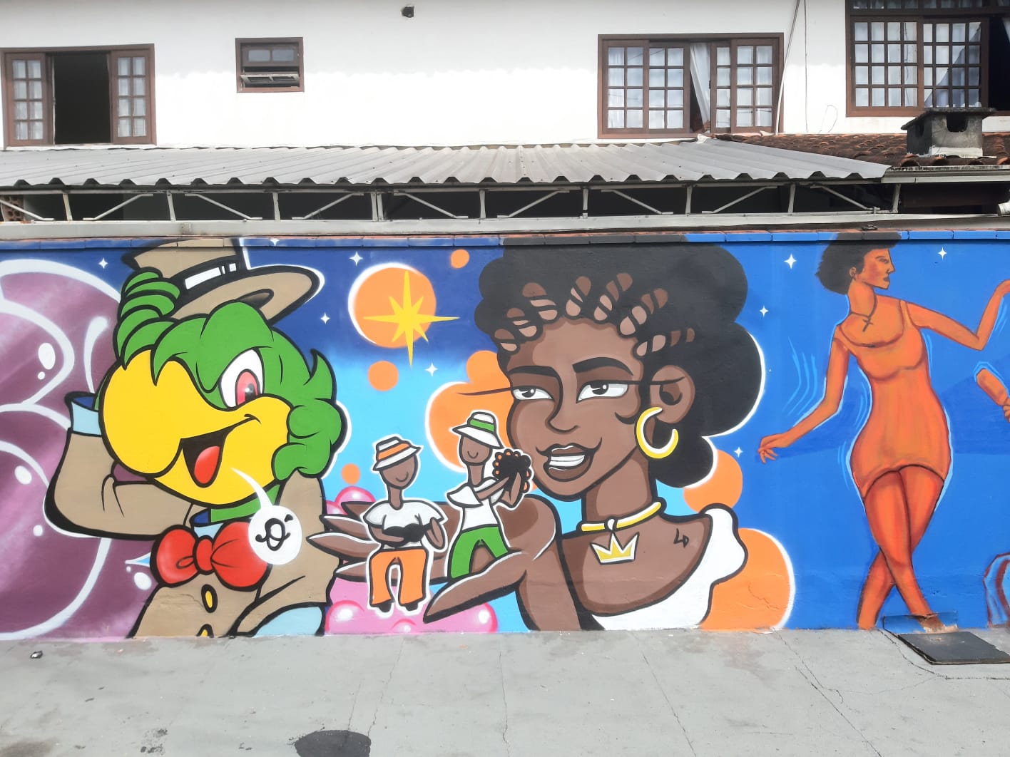 Trecho de mural urbano com personagens ilustrados, incluindo figura inspirada no Zé Carioca e representações artísticas em cores vibrantes 